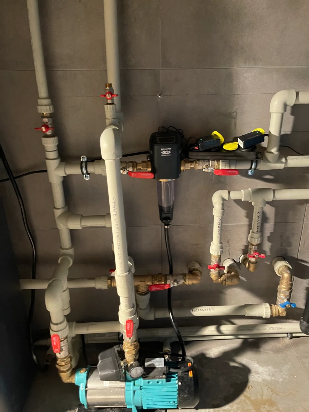 Widoczna instalacja hydrauliczna z pompą, filtrami i zaworami kulowymi na ścianie pomieszczenia technicznego – Instalacje hydrauliczne