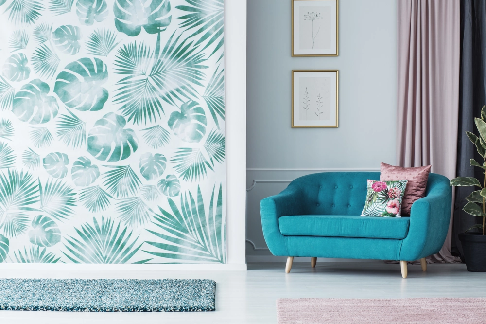 Salon z tropikalną tapetą na ścianie, turkusowa sofa, poduszki i rośliny – Tapetowanie
