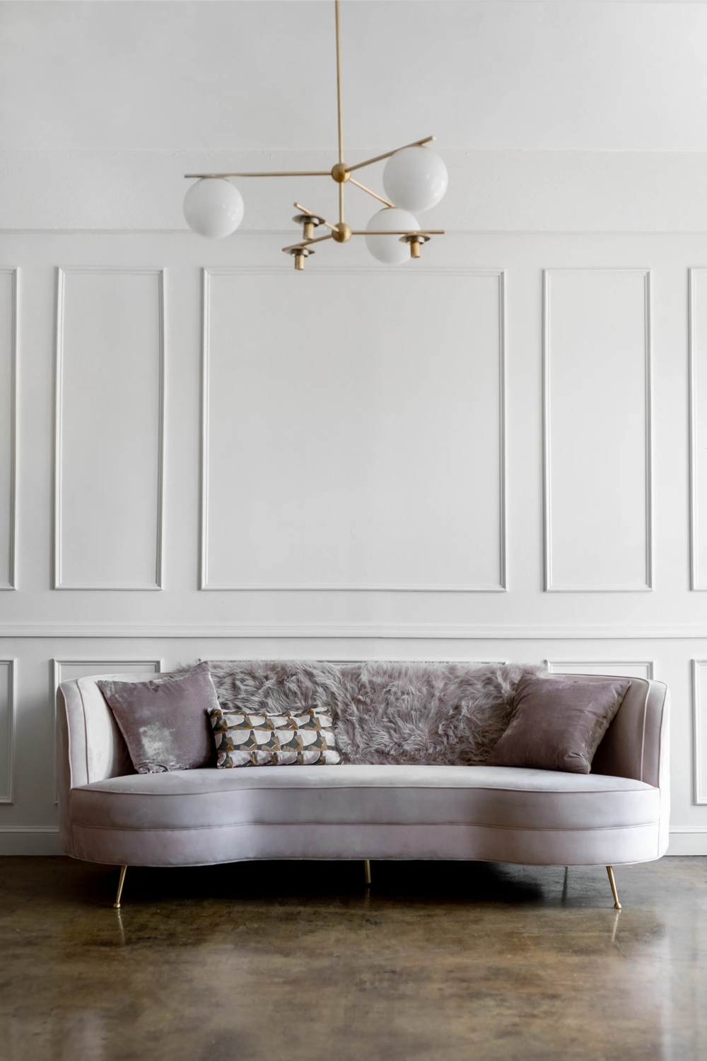 Welurowa sofa na tle białej ściany z ozdobną sztukaterią i złotą lampą sufitową, Sztukateria